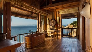 A wooden cabin with a large bathtub, wooden furniture, and a view of the ocean.