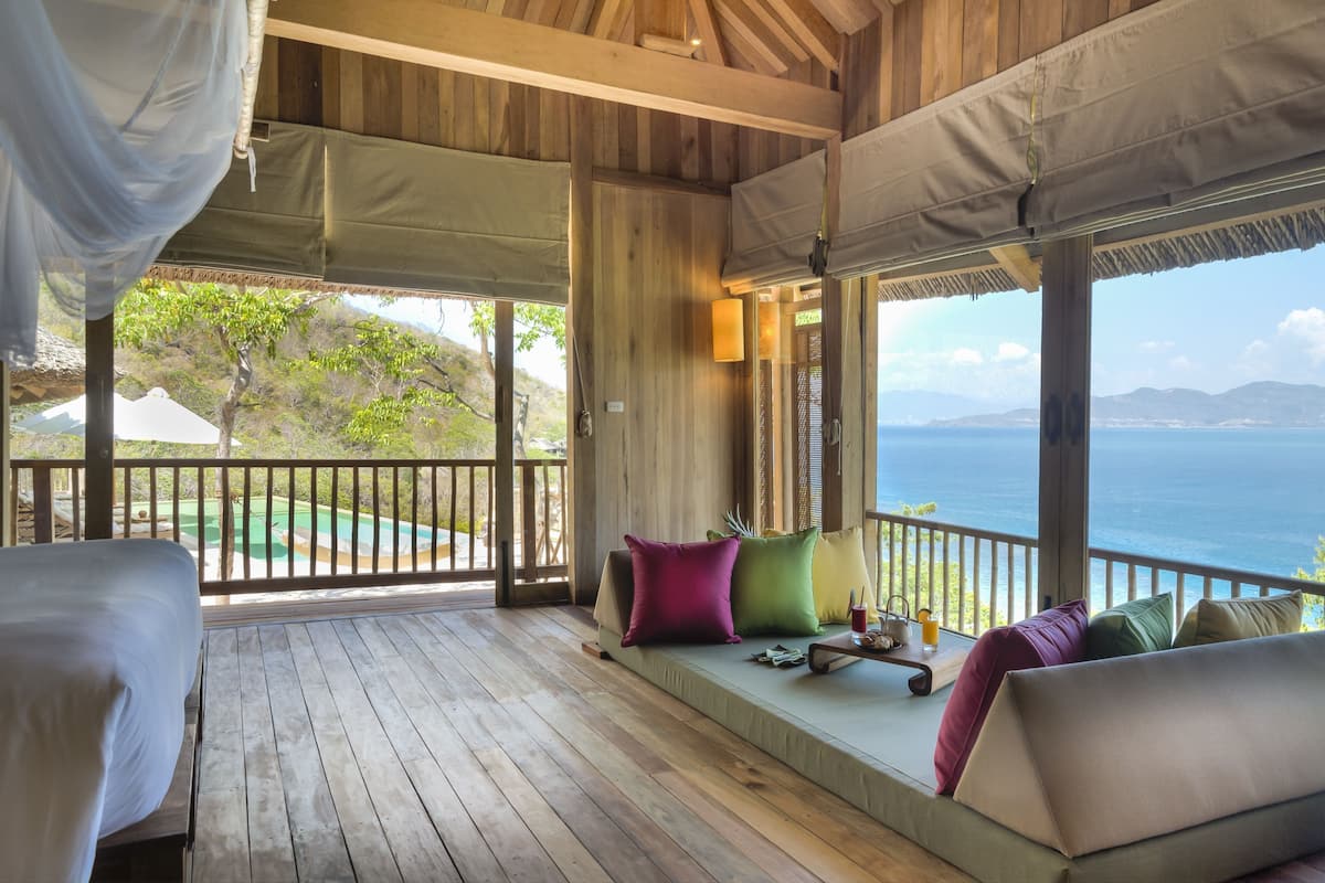 Una terraza de madera con un sofá y cojines, vista al mar y una piscina al fondo.