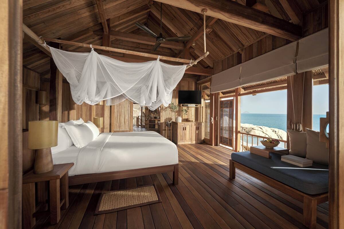 A wooden cabin with a bed, a TV, and a view of the beach.