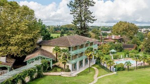 A two-story building with a swimming pool, surrounded by lush greenery and a clear sky.