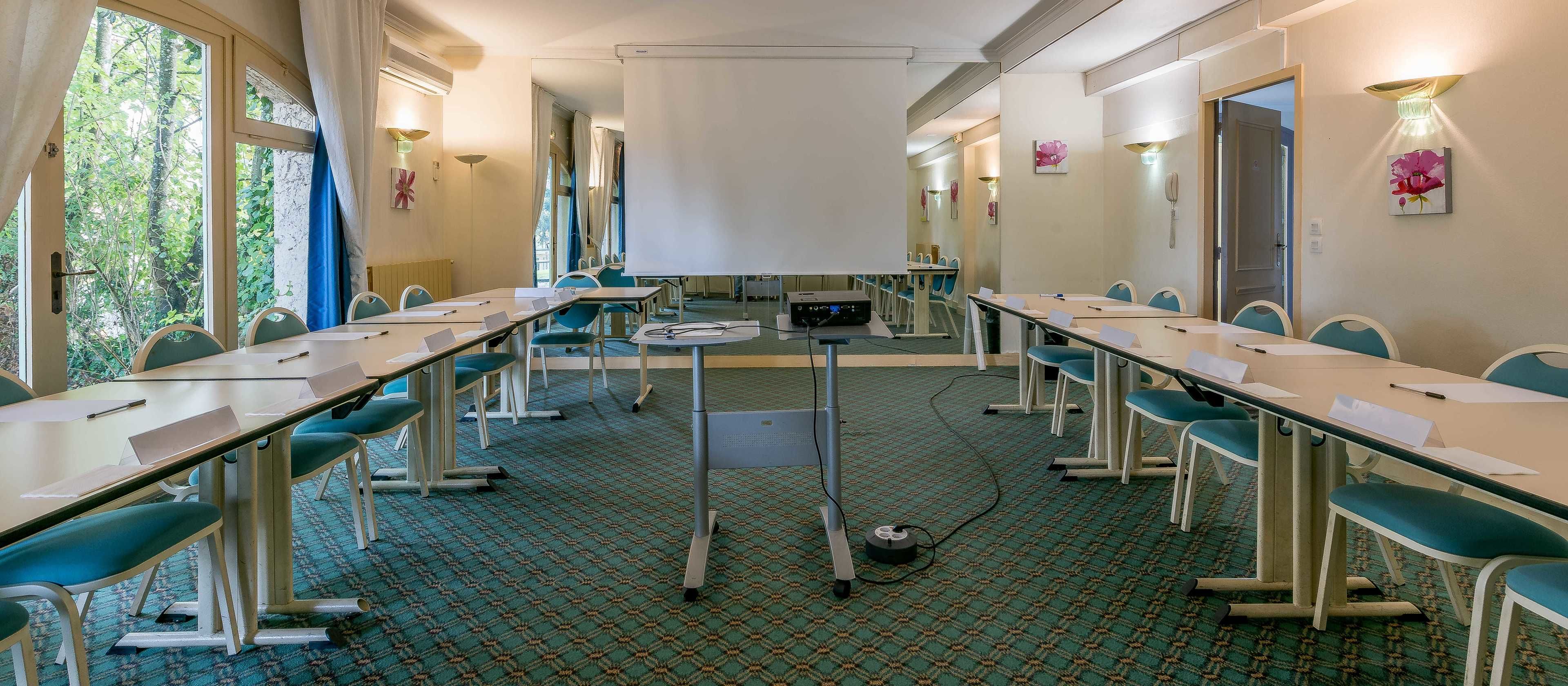 A conference room with a long table, chairs, a projector screen, and a carpeted floor.