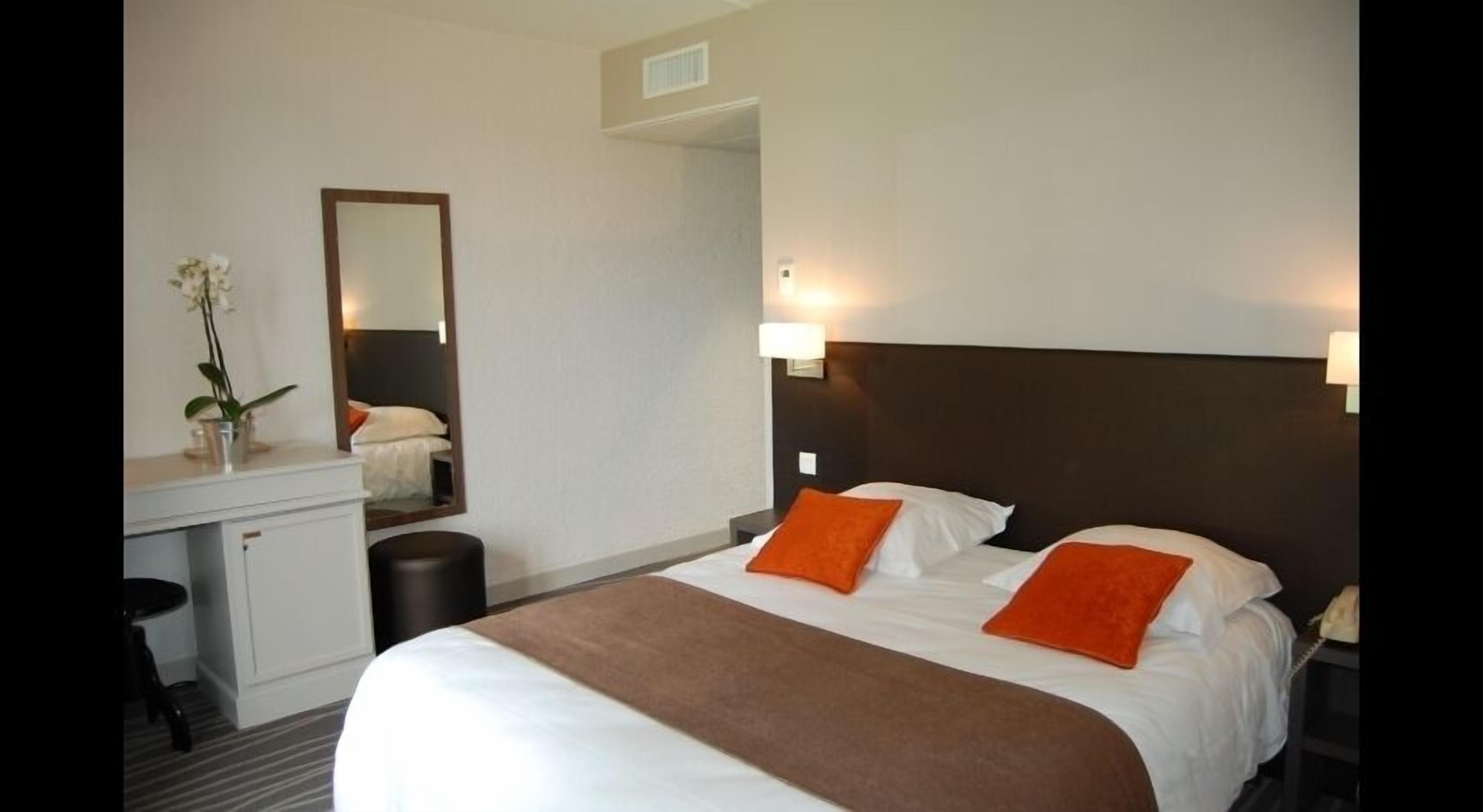 A hotel room with a bed, bedside tables, a mirror, and a desk with a lamp.