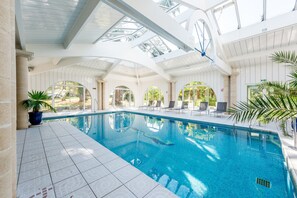 An indoor swimming pool with clear blue water, surrounded by white tiled flooring and columns. - Logis Hôtels- Hôtel et Restaurant Domaine de Fompeyre (Bazas)