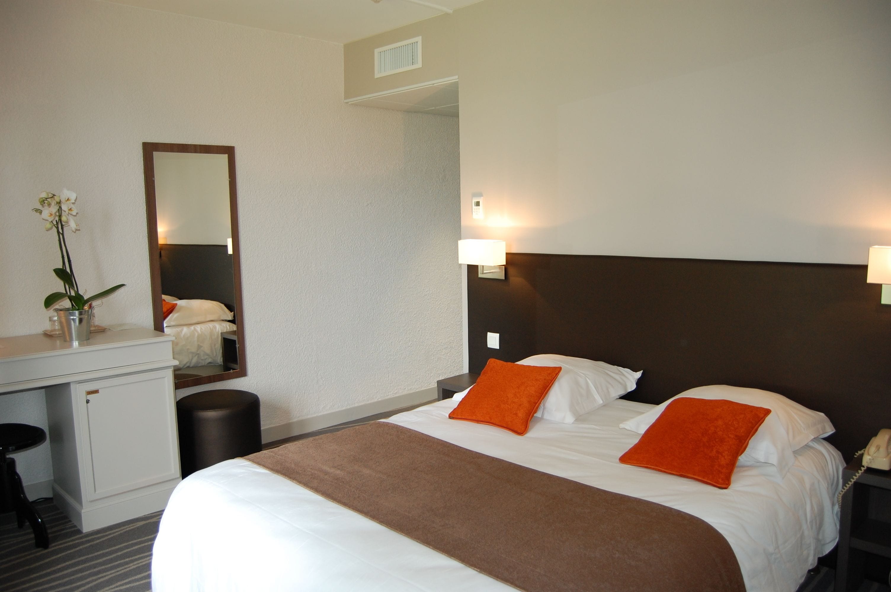 A hotel room with a bed, bedside lamps, a desk, a mirror, and a telephone.