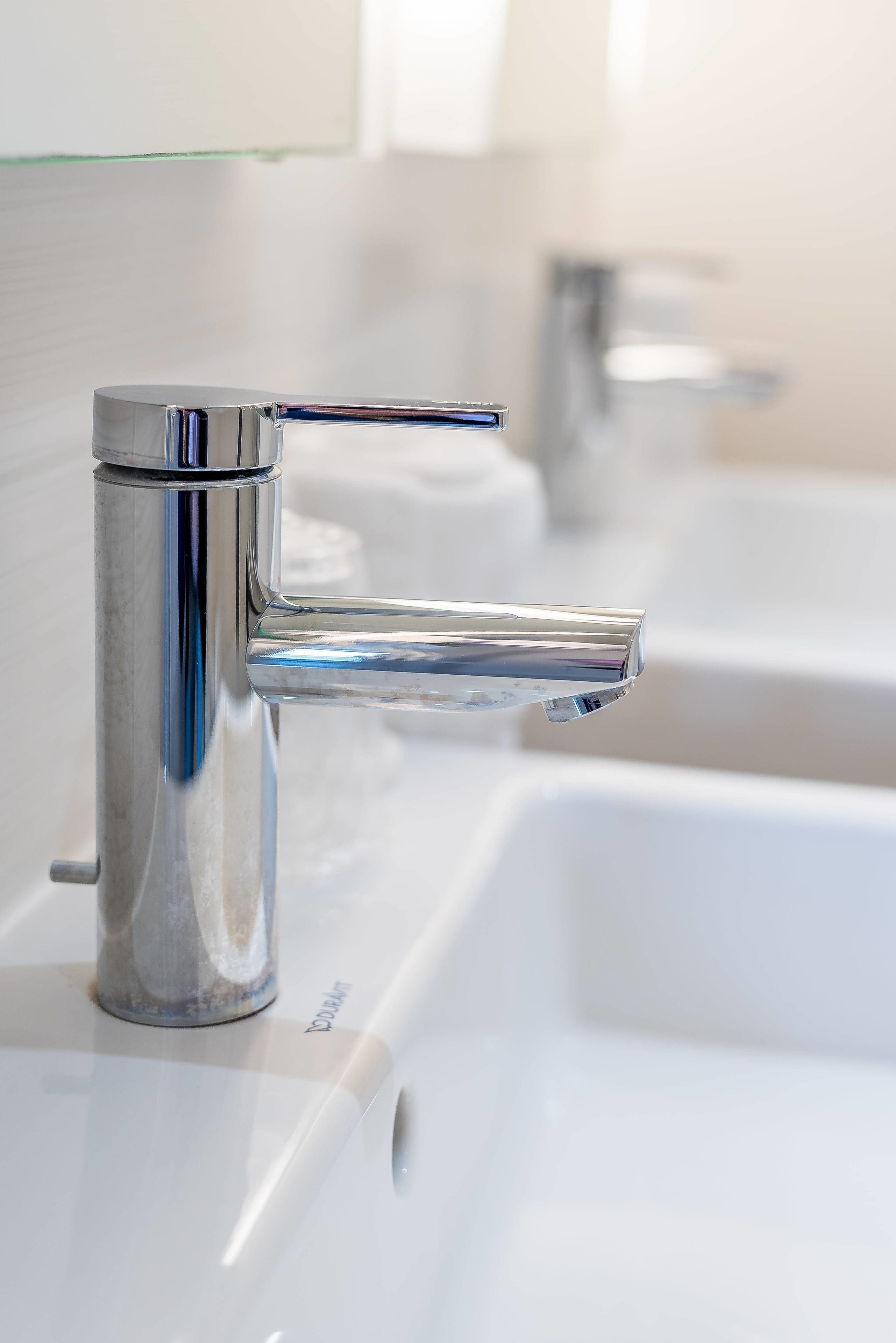 Een moderne badkamer met een chromen kraan, een glazen douchecabine en een witte wasbak.