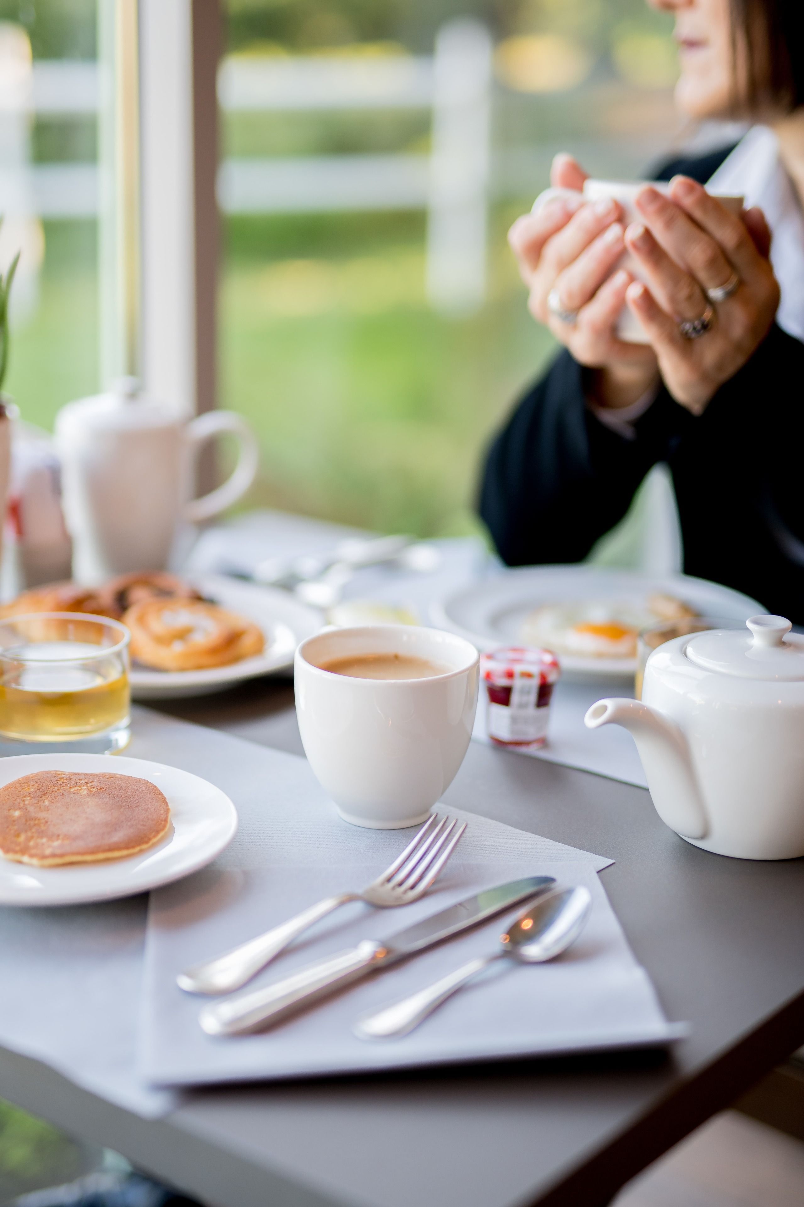 Une table mise pour le petit-déjeuner, avec une nappe, de l’assiette, une théière, des tasses et des couverts.
