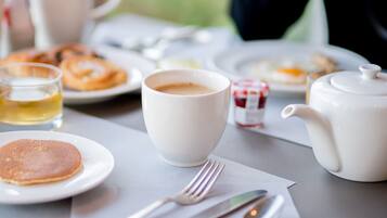 Une table mise pour le petit-déjeuner, avec une nappe, de l’assiette, une théière, des tasses et des couverts.
