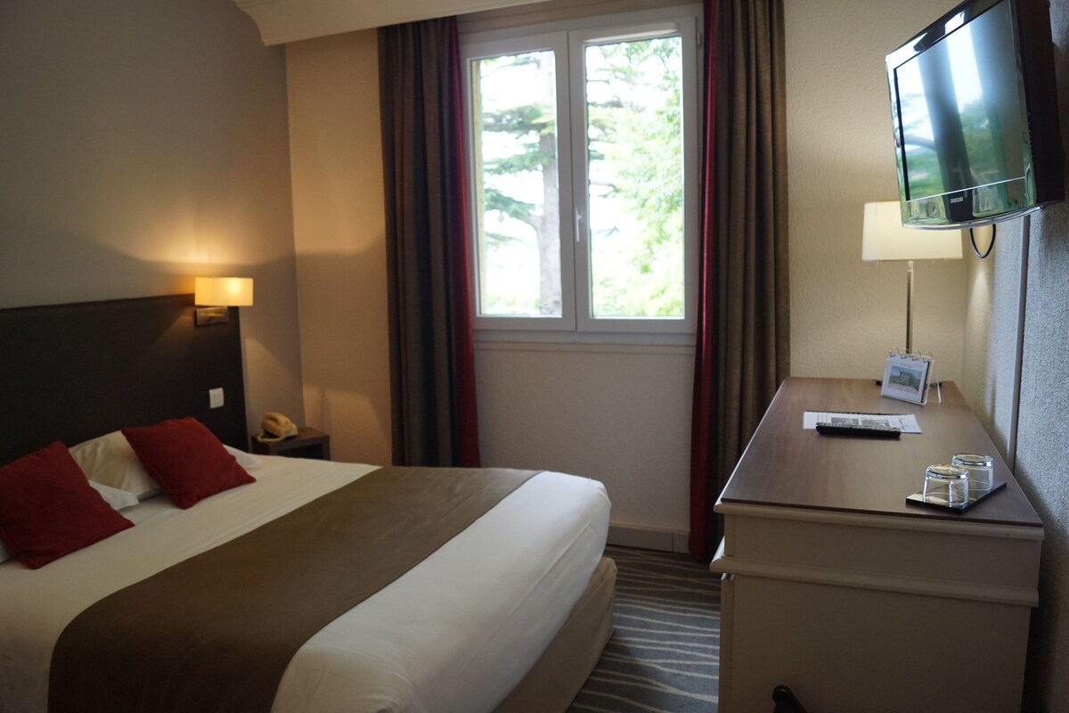 A hotel room with a bed, a desk, a TV, a lamp, and a window with curtains.