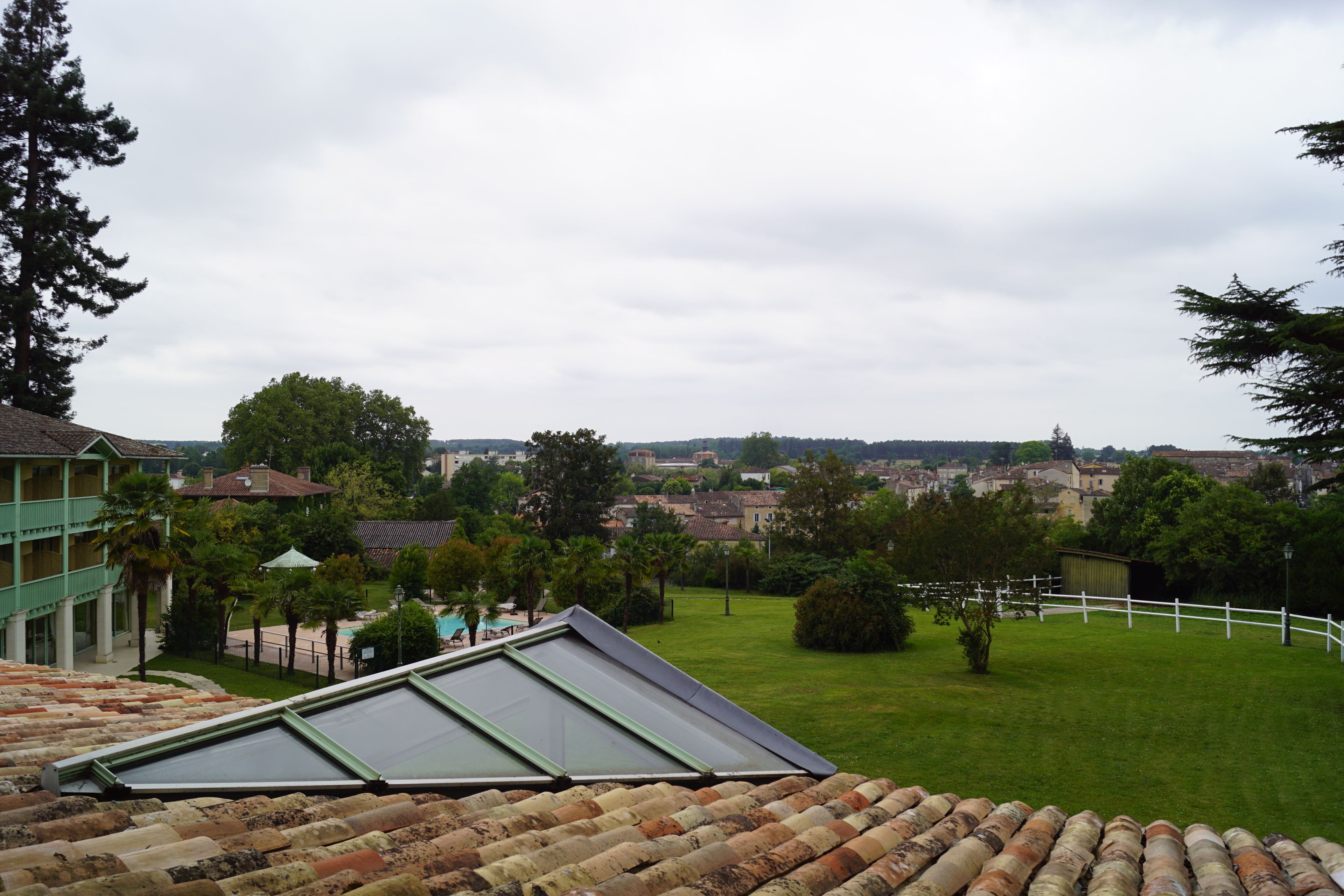 A view from a rooftop terrace with a green building, a grassy lawn, and a distant townscape.