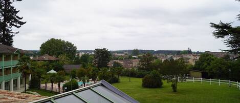 A view from a rooftop terrace with a green building, a grassy lawn, and a distant townscape.
