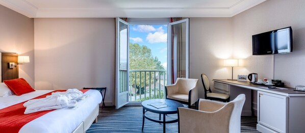 A hotel room with a bed, a desk, a chair, a TV, and a balcony with a view.