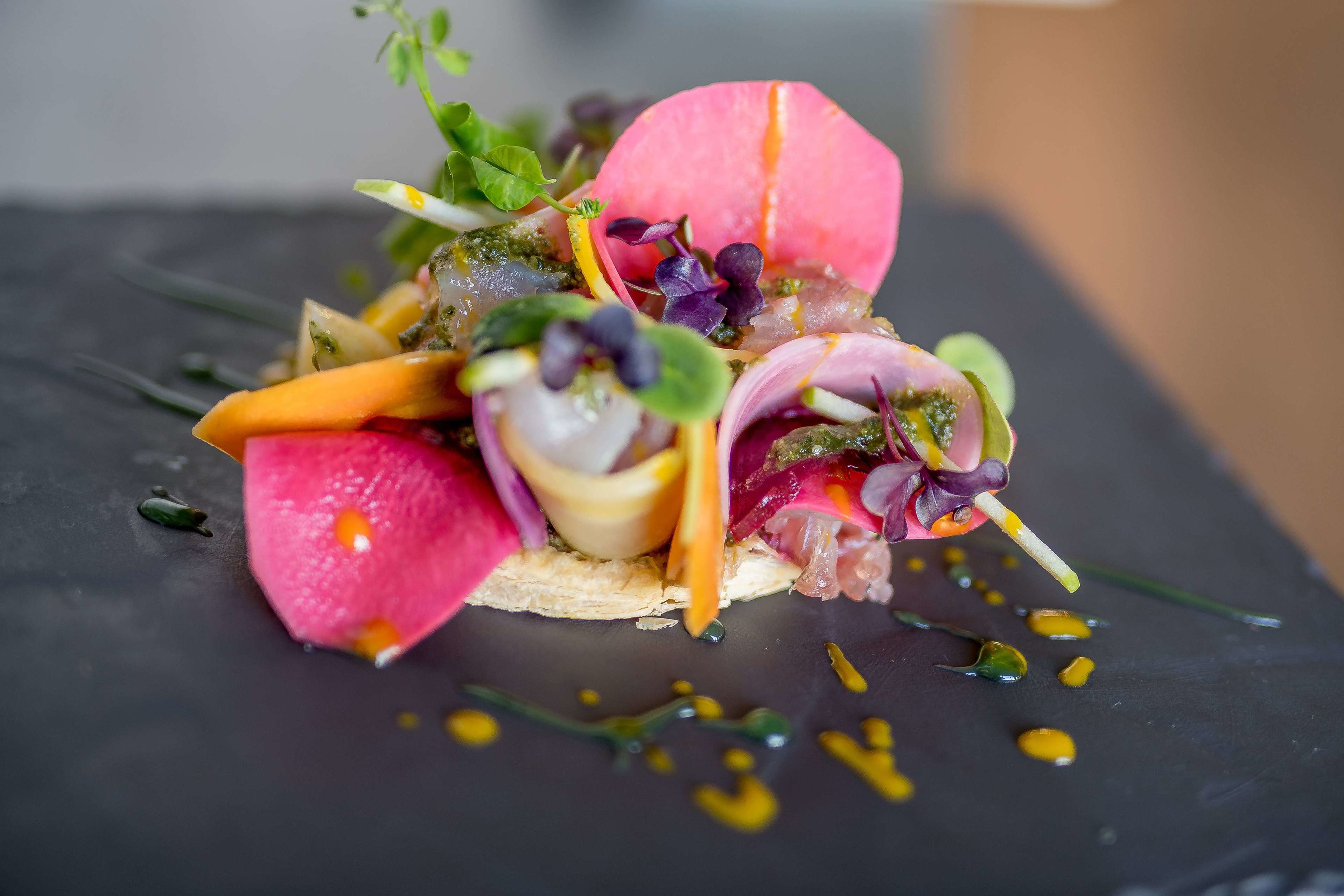 A gourmet dish with various vegetables and garnishes on a slate plate.