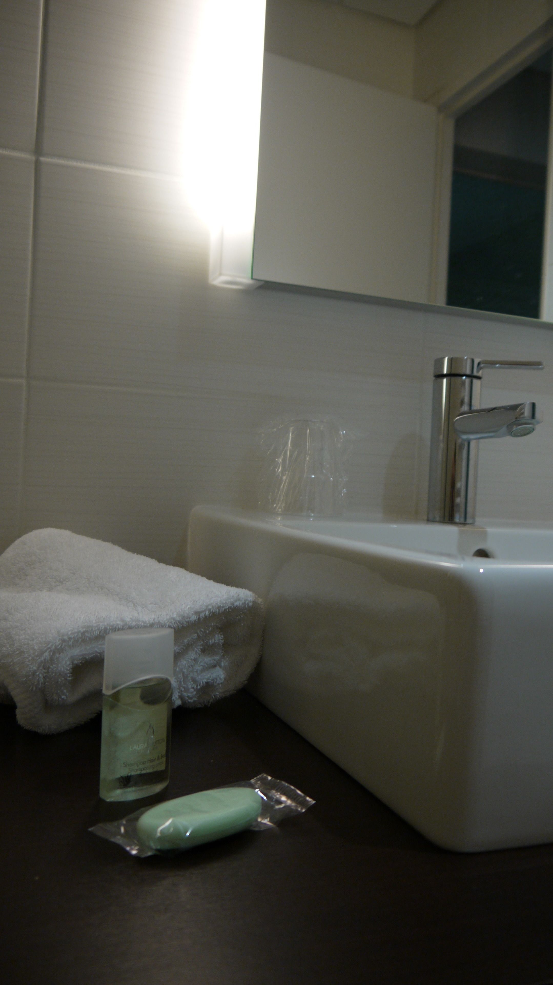 Un baño con un lavabo blanco, una toalla, una botella de champú y una pastilla de jabón.