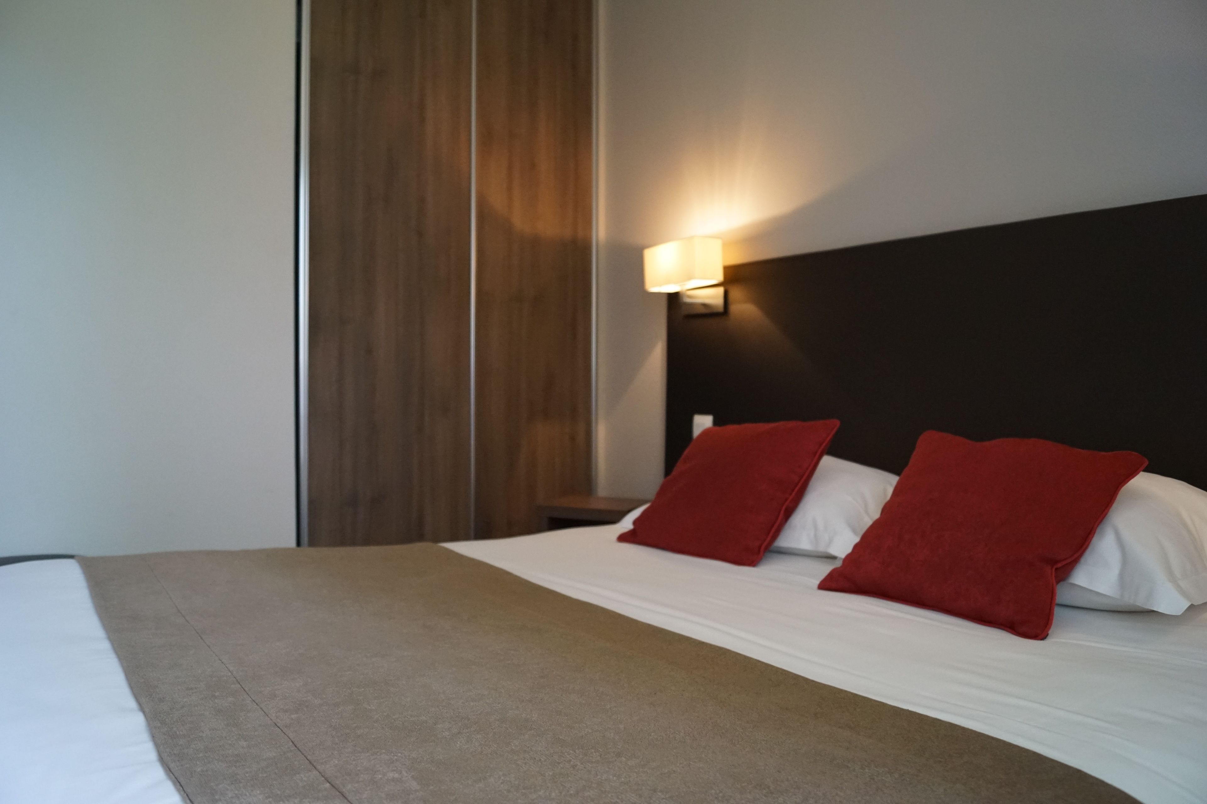 Une chambre d’hôtel avec un lit, une table de chevet et une lampe fixée au mur.