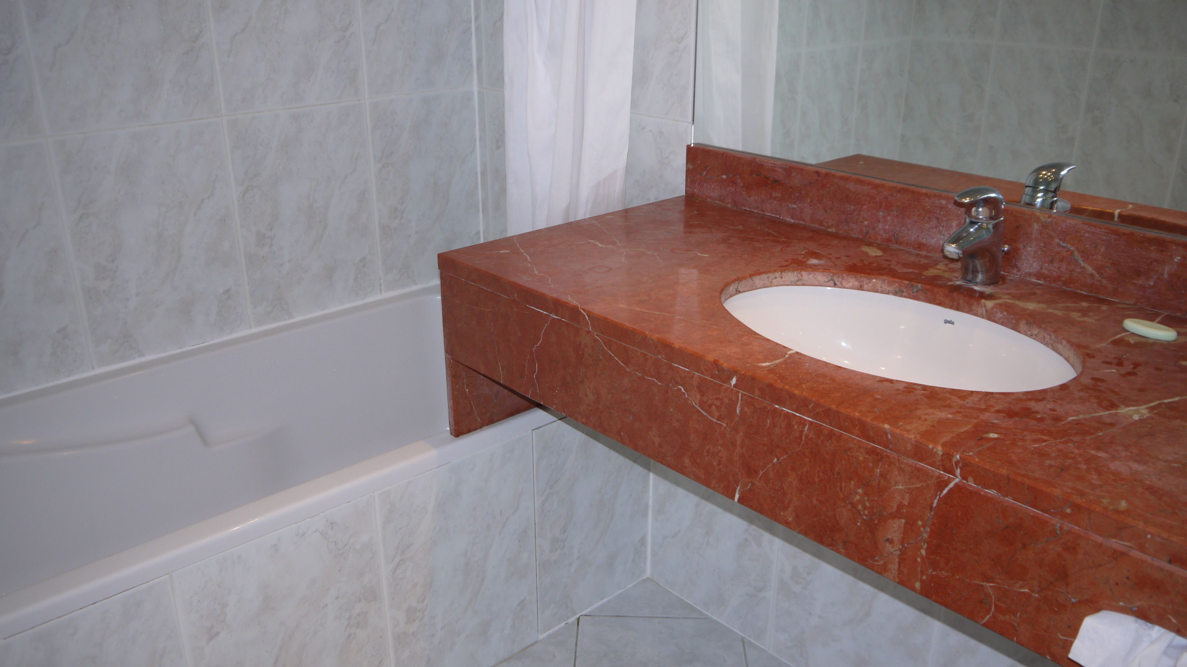 A bathroom with a marble sink, a mirror, and a bathtub.