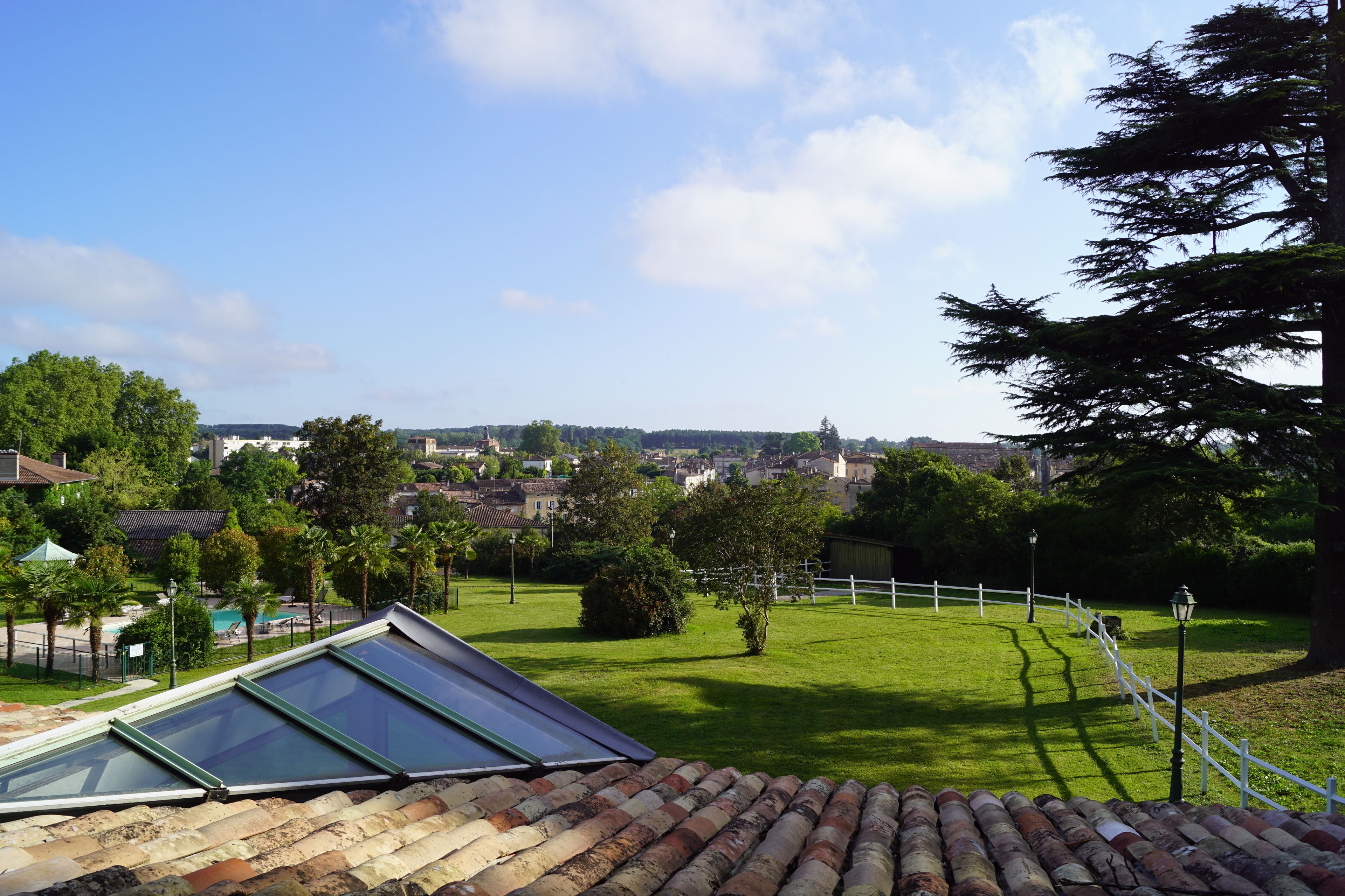 A view from a rooftop with a glass skylight, a white fence, and a green lawn.