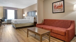 Habitación de hotel con cama, sofá rojo, mesa de madera, escritorio con silla y ventana con cortinas.