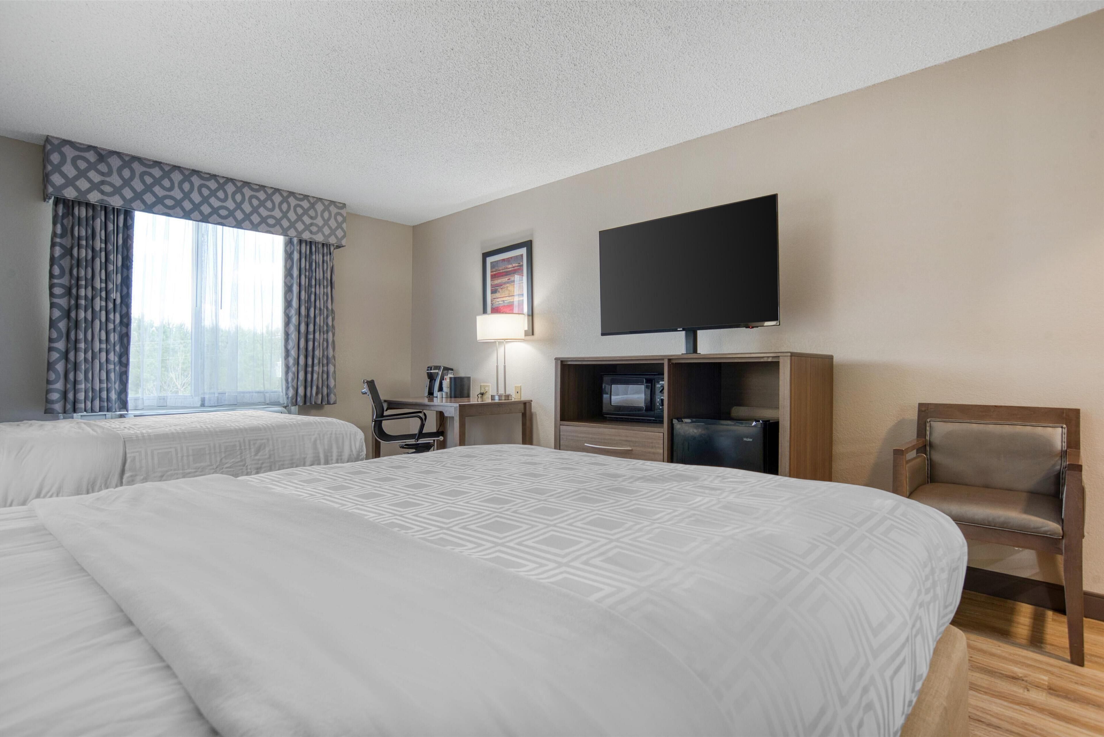 A hotel room with two beds, a desk, a chair, a TV, and a microwave.