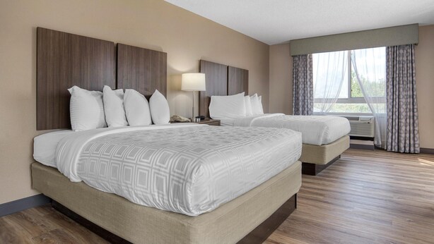 Una habitación de hotel con dos camas, una mesita de noche, una lámpara y una ventana con cortinas.