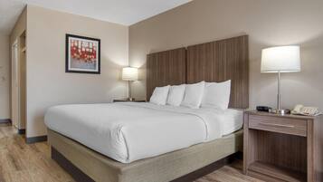 A hotel room with a large bed, two bedside tables with lamps, a wooden headboard, and a framed picture on the wall.