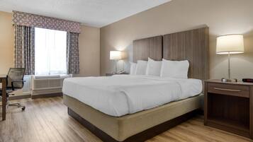 Ein Hotelzimmer mit einem großen Bett, einem Schreibtisch mit Stuhl, einem Nachttisch mit Lampe und einem Fenster mit Vorhängen.