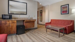 Un espacio habitable compacto con kitchenette, un sofá rojo, una mesa de centro y un espejo grande.