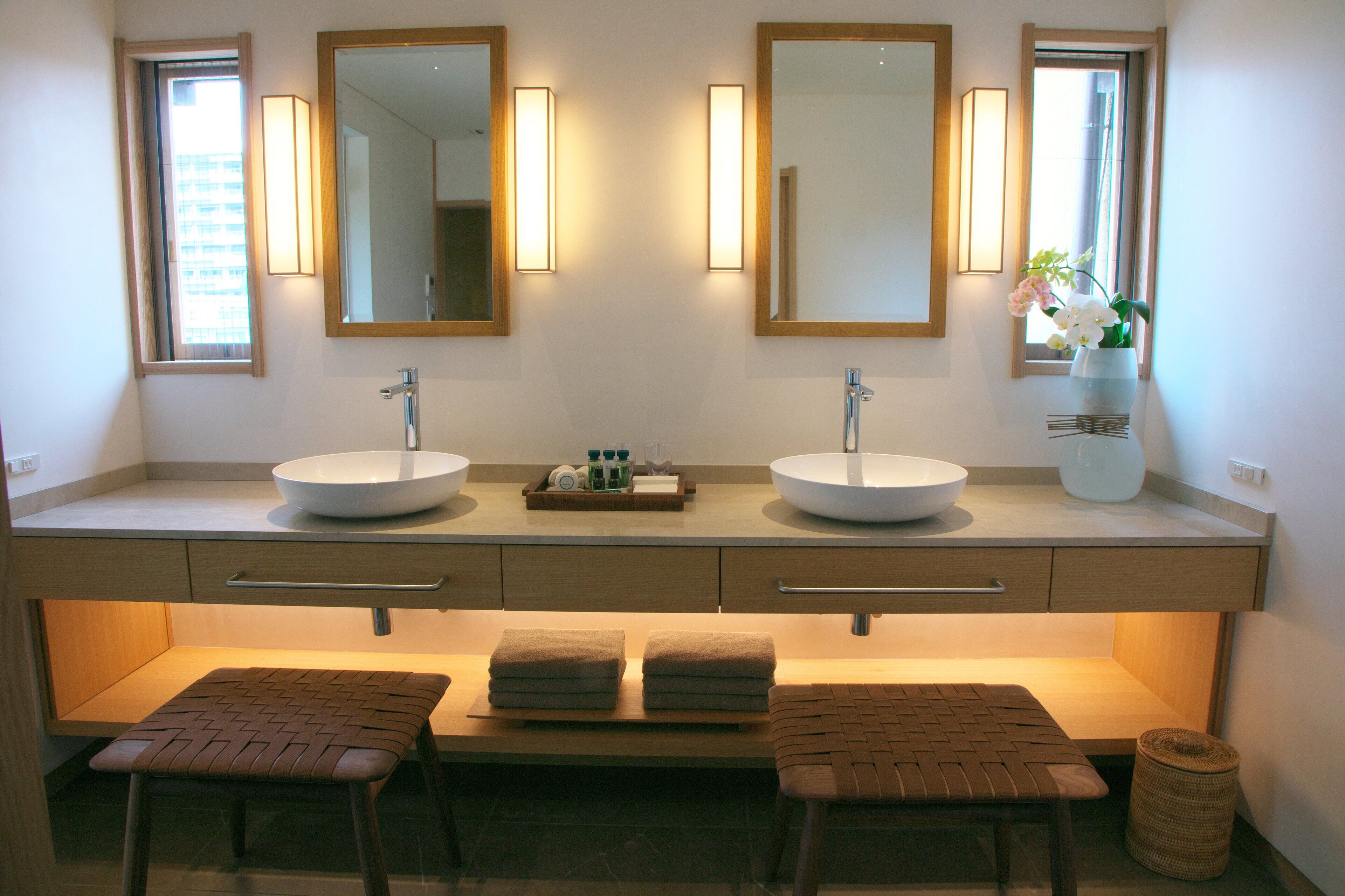 A modern bathroom with two sinks, mirrors, and a bench with towels.