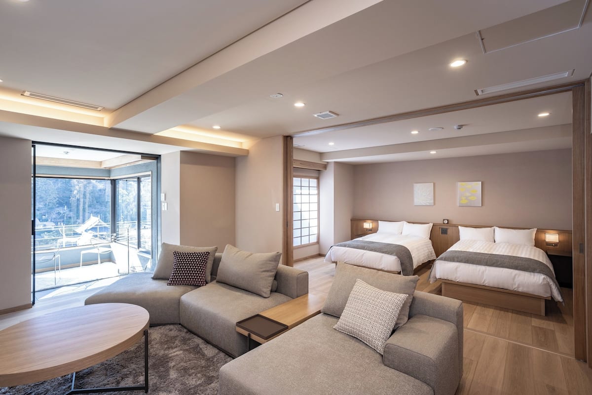 Une chambre d’hôtel moderne avec un canapé, deux lits, une petite table et une vue sur l’extérieur.