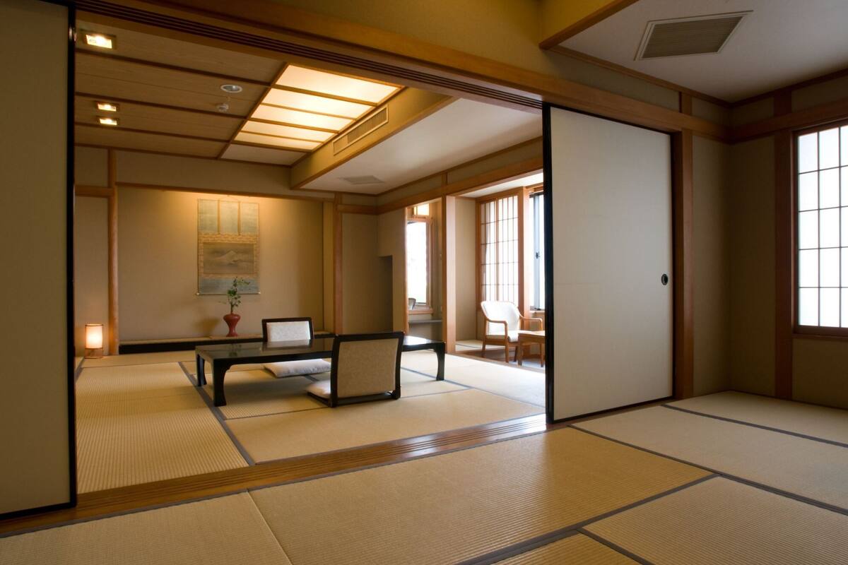 Une pièce de style japonais traditionnel, avec un sol recouvert de tatamis, une table basse, une chaise et des portes coulissantes.