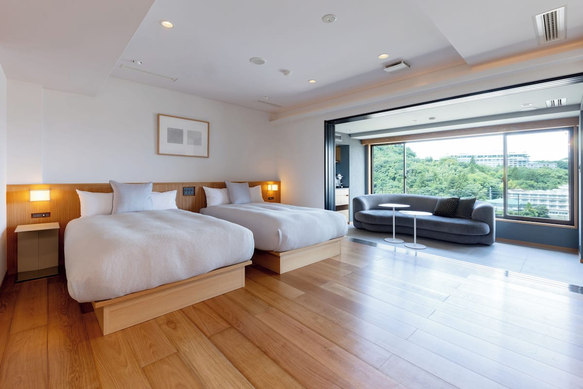Une chambre d’hôtel moderne avec deux lits, un canapé et une grande fenêtre donnant sur la ville.