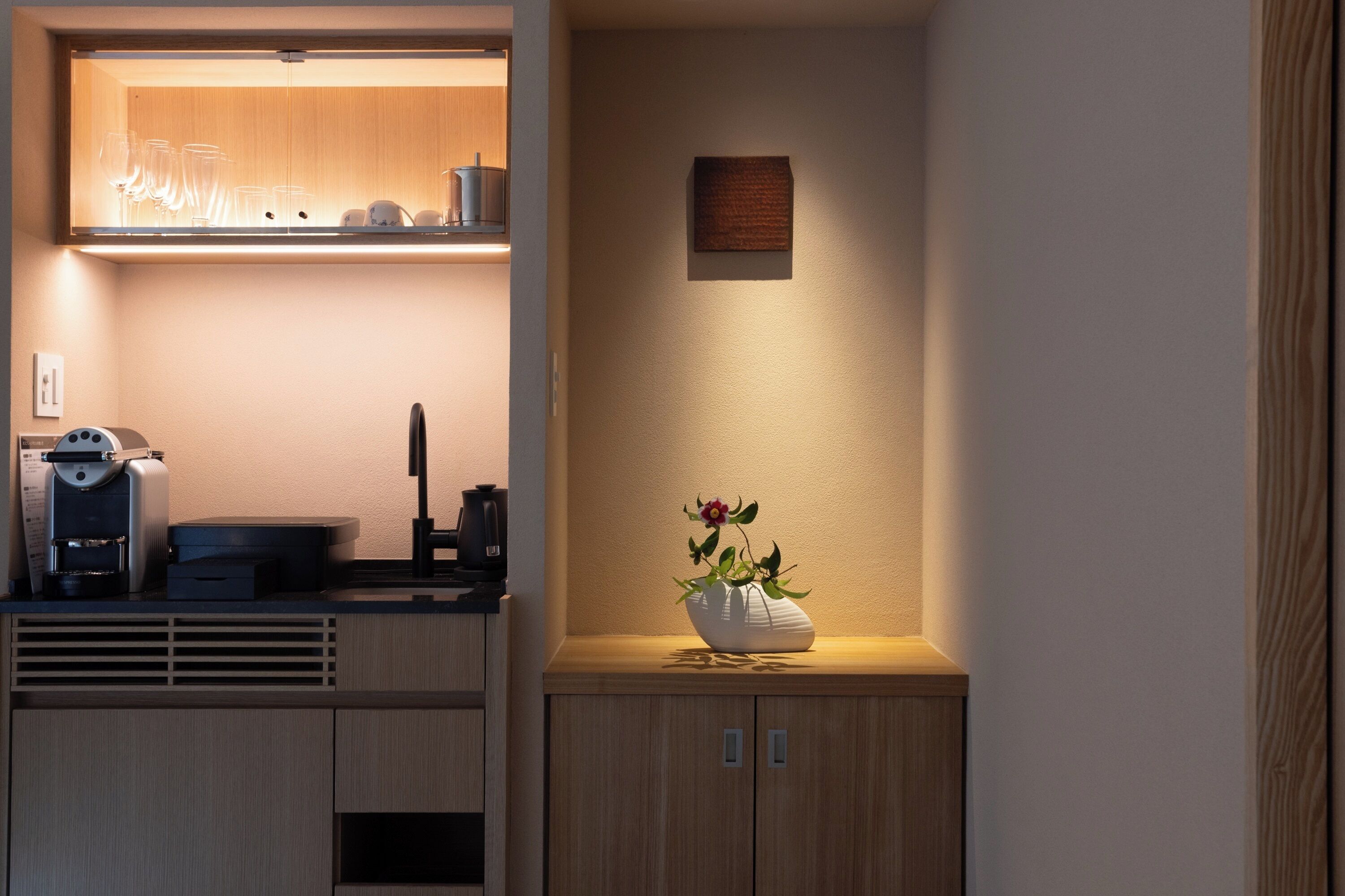 A modern kitchen with a built-in coffee machine, a kettle, and a vase with flowers on the counter.