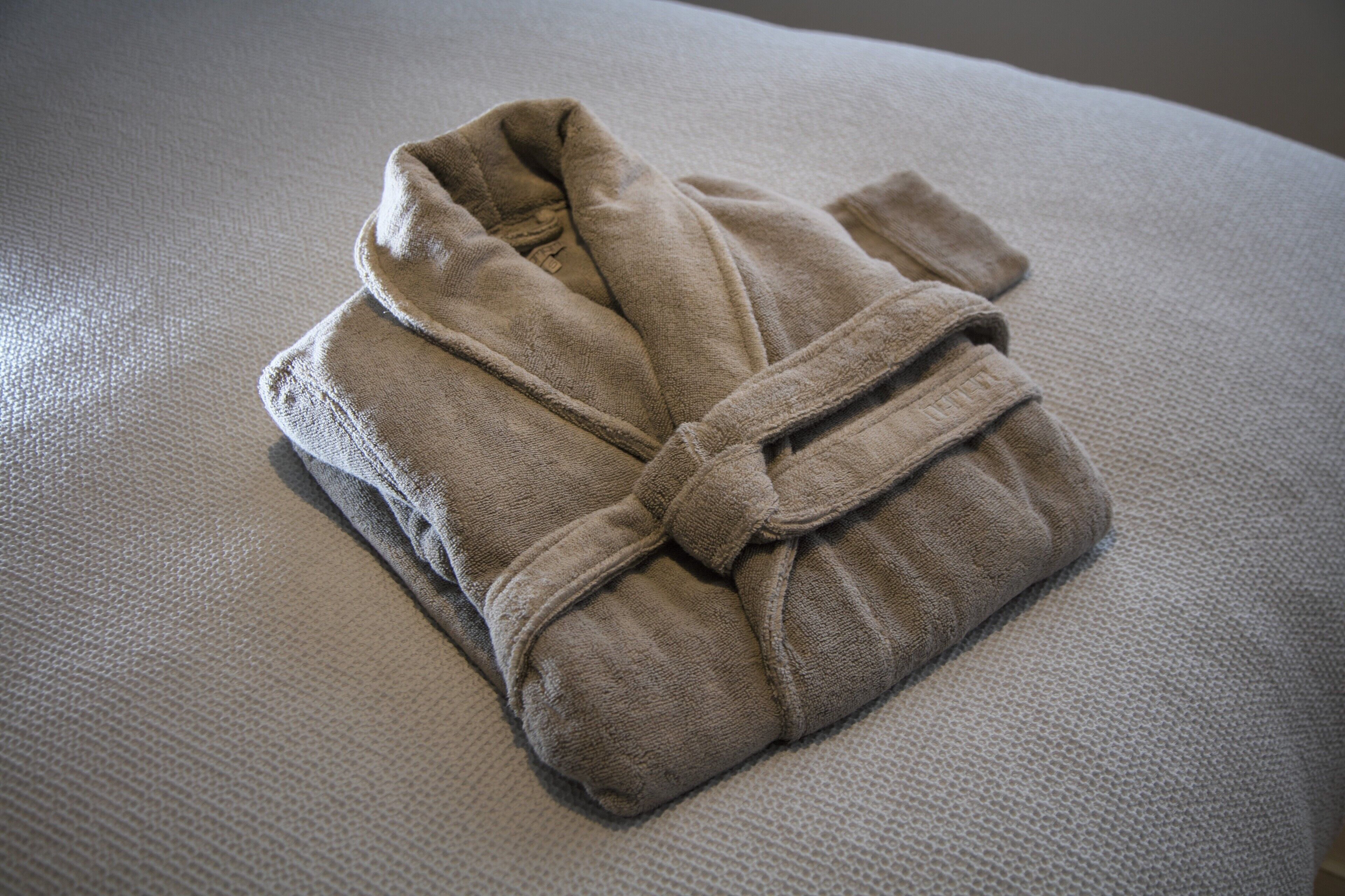 A neatly folded beige bathrobe on a textured gray surface.