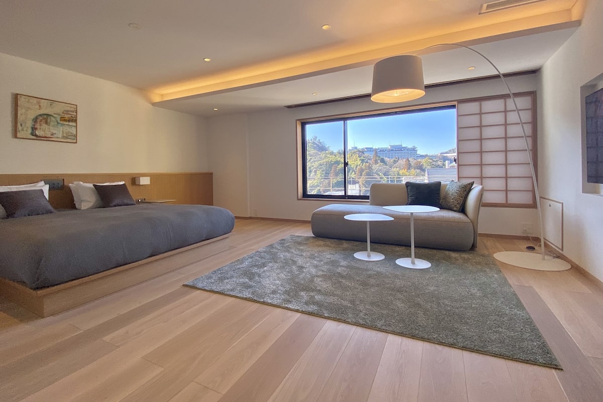 Une chambre d’hôtel moderne avec un grand lit, un canapé, une petite table et une vue sur la ville.