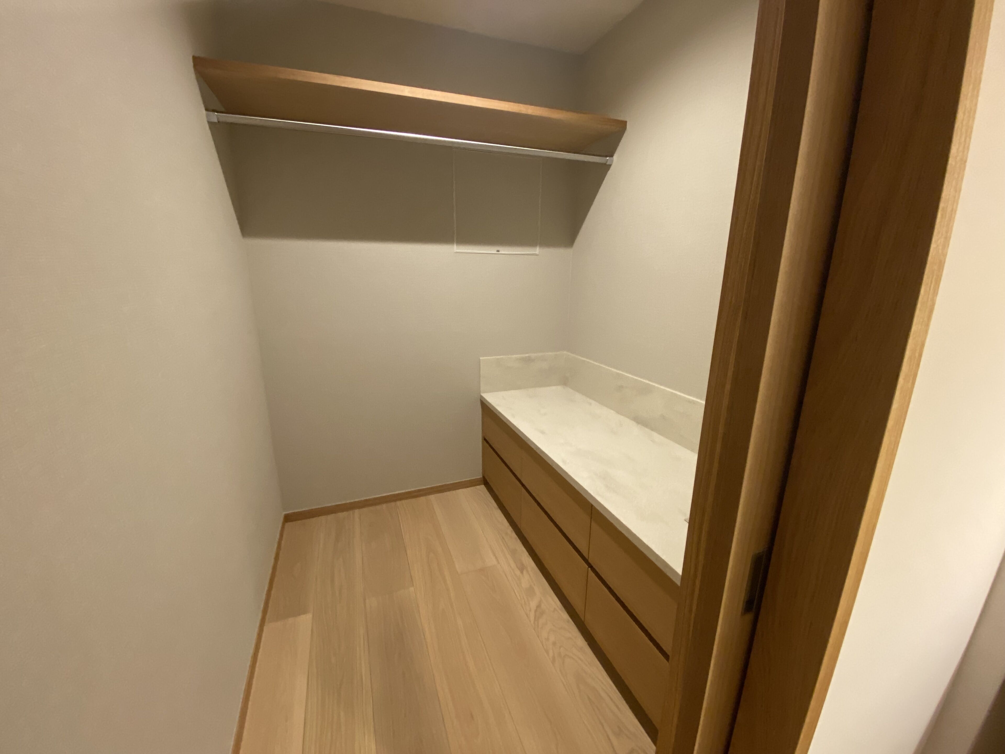 A small, narrow room with a wooden floor, a white countertop, and a wooden shelf above.