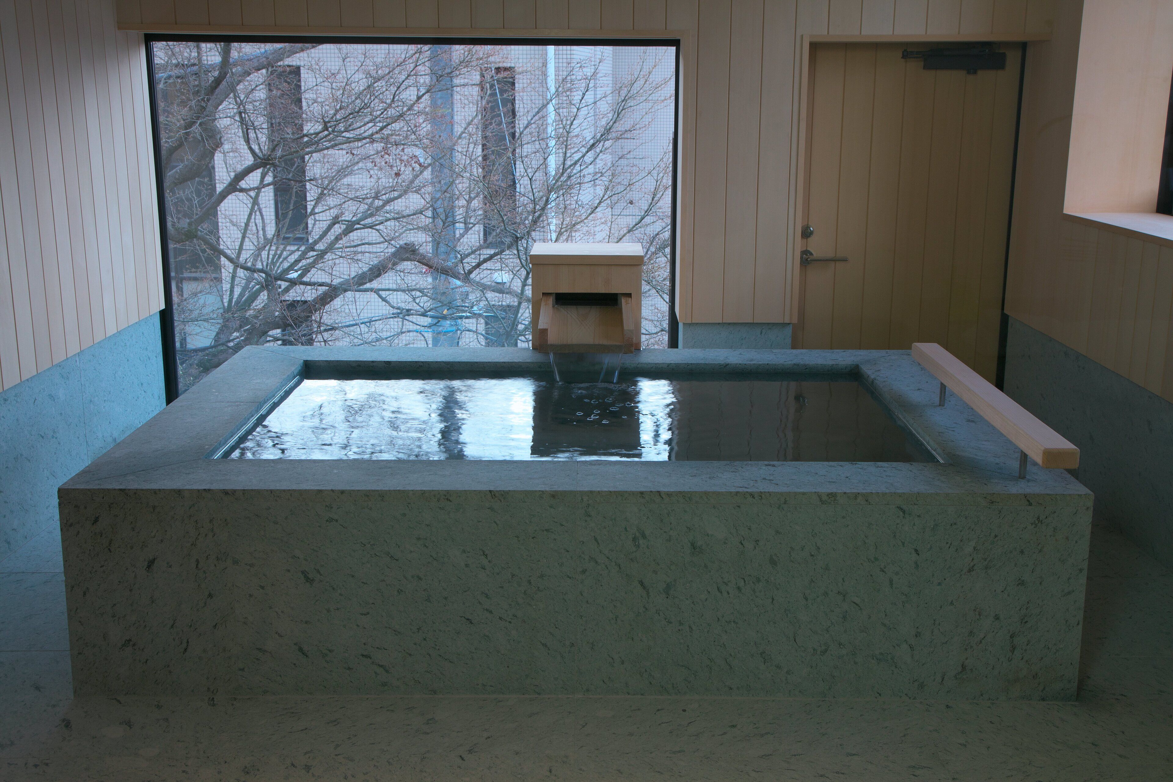 Een stenen jacuzzi met een houten bankje en een klein houten bouwwerk in het midden.
