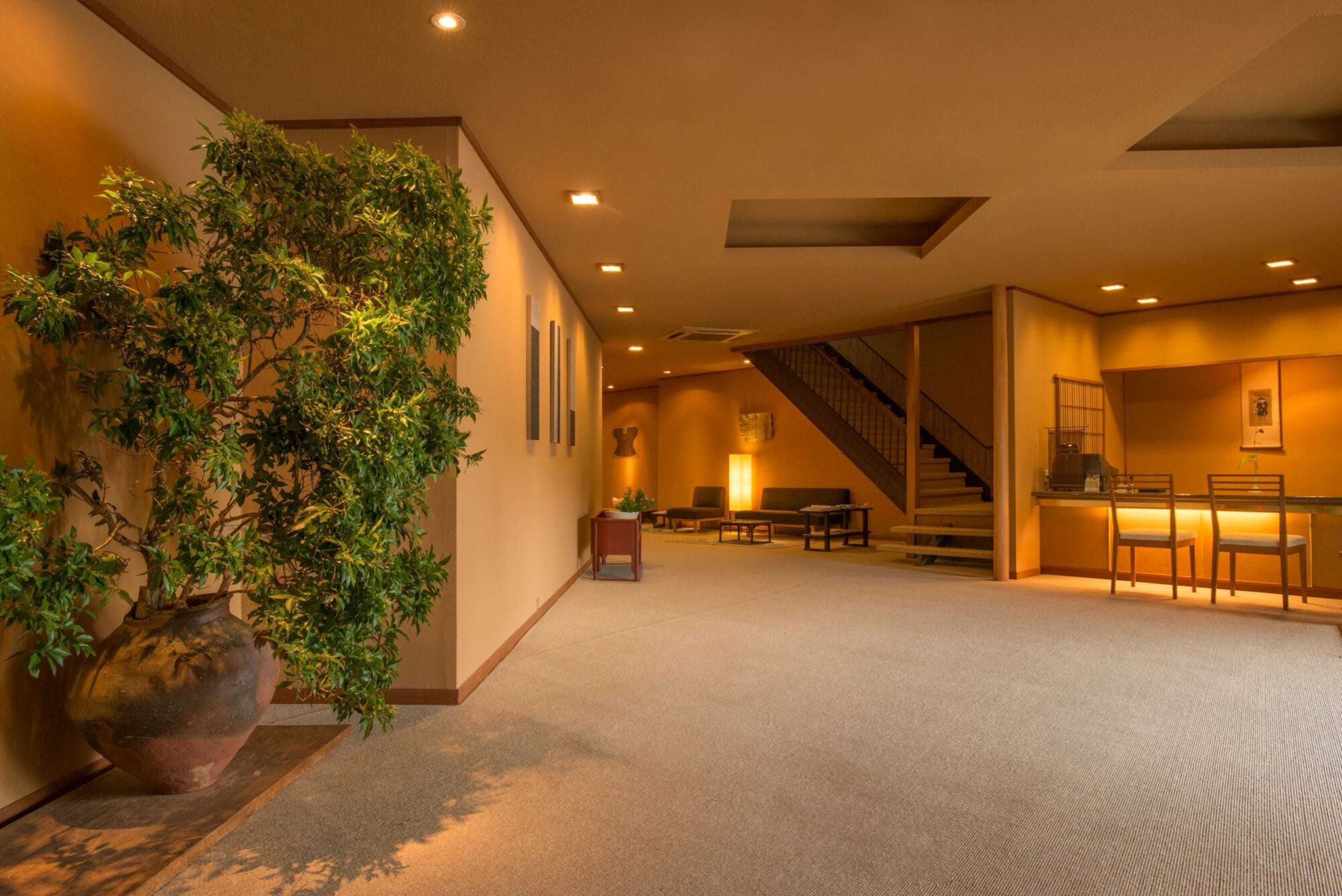 A spacious lobby with a large potted plant, a staircase, and a reception desk.