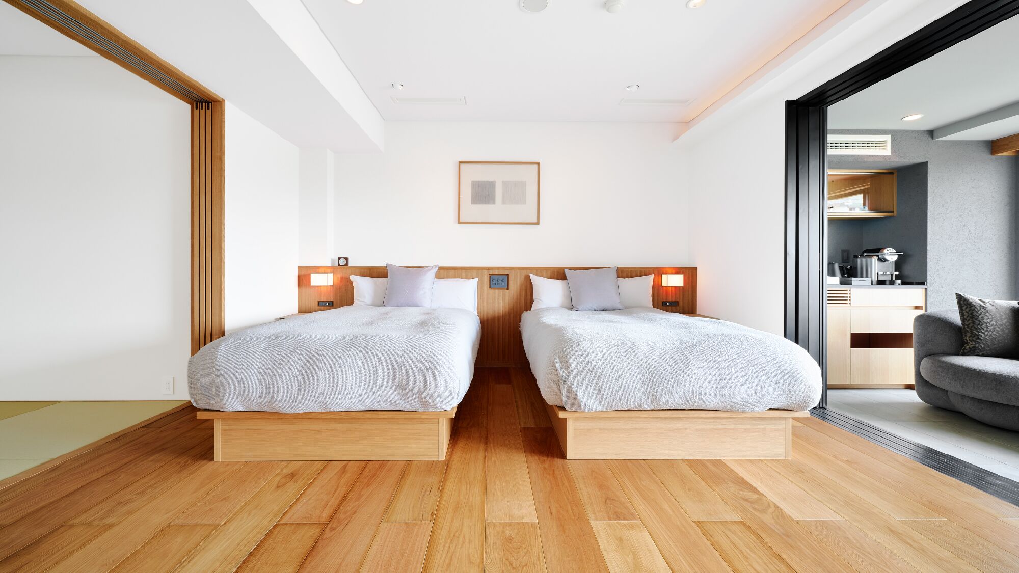Habitación de hotel con dos camas, suelo de madera, kitchenette y vistas a través de un ventanal.