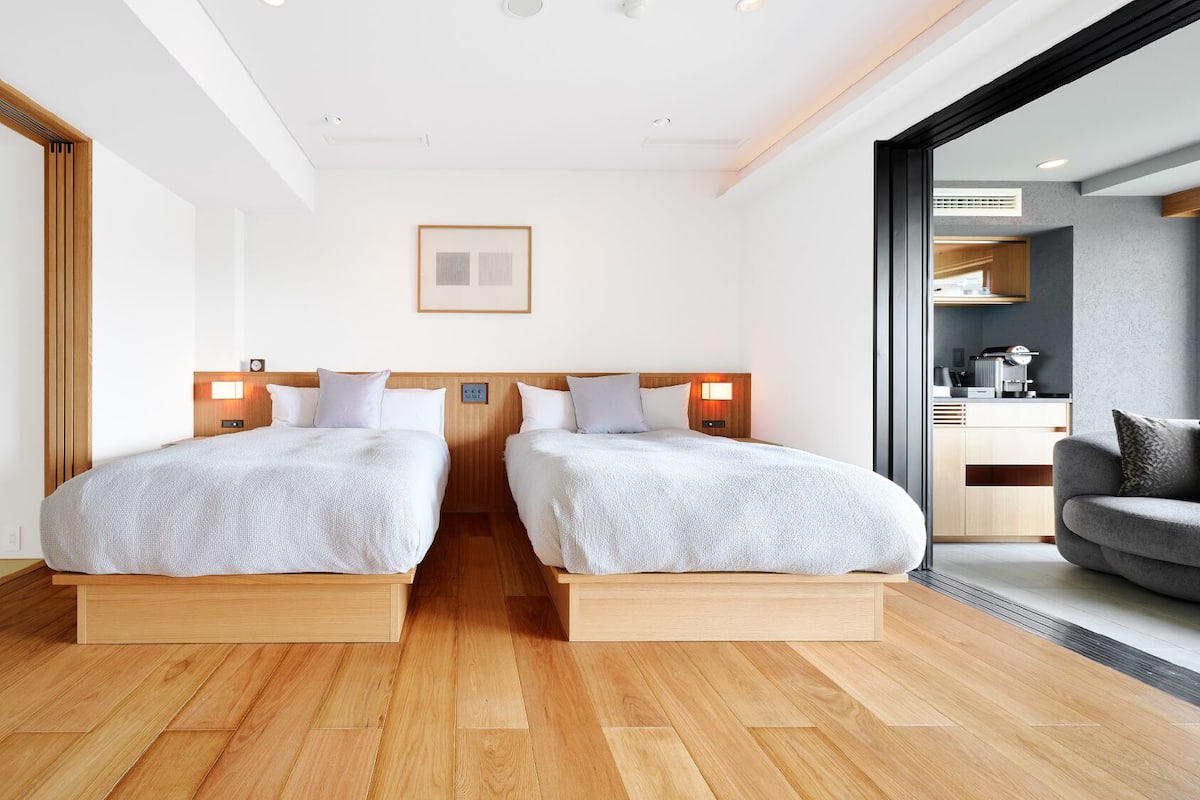 Une chambre d’hôtel avec deux lits, un plancher en bois, une kitchenette et une vue sur l’extérieur grâce à une porte vitrée.