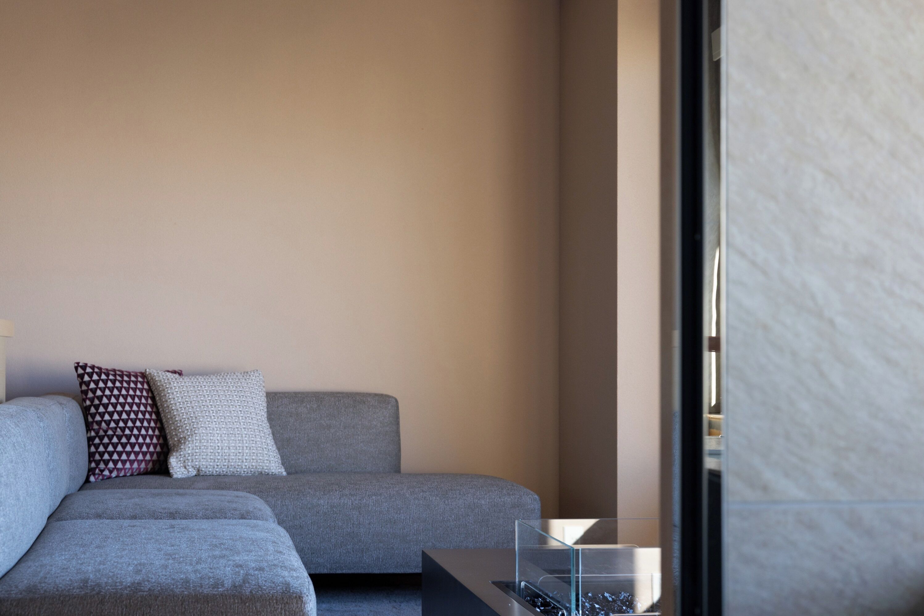 Un salon moderne avec un canapé gris, des coussins à motifs et une table basse en verre.