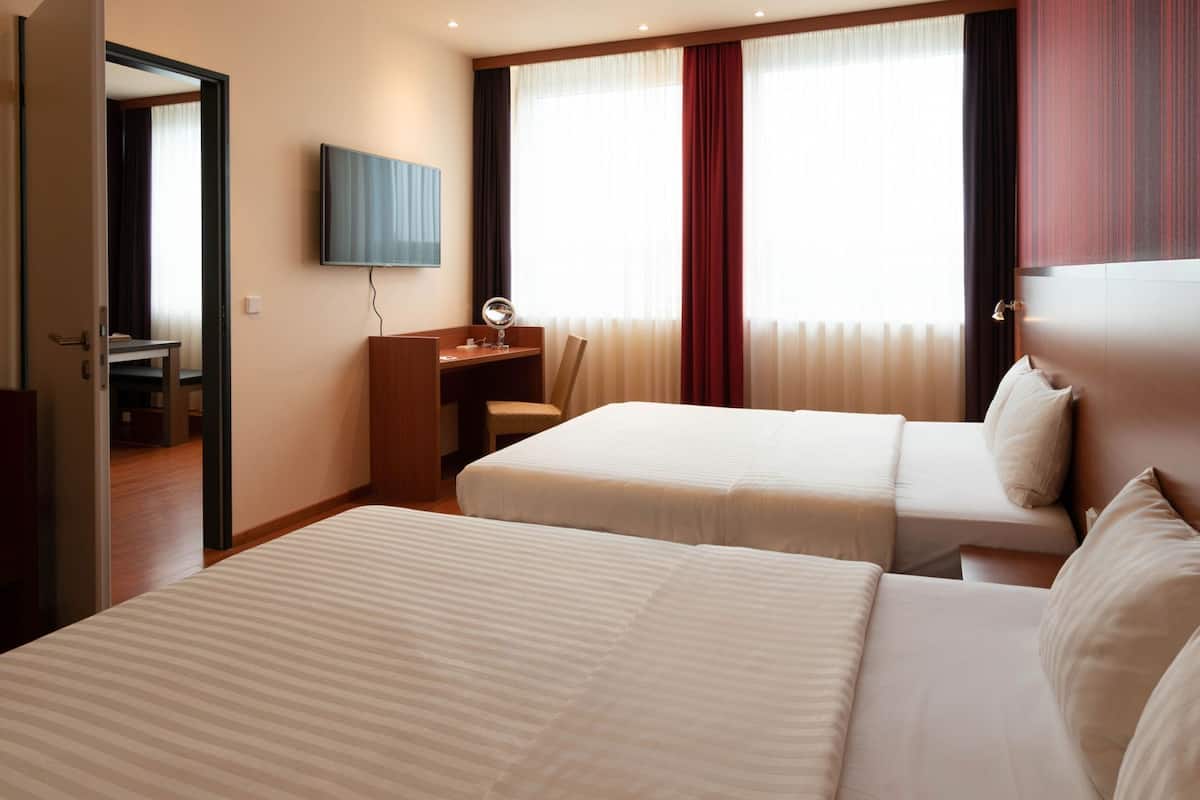A hotel room with two beds, a desk with a mirror, a TV, and a window with curtains.