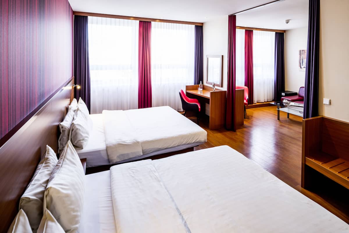 A hotel room with two beds, a desk, a chair, and a large window with curtains.