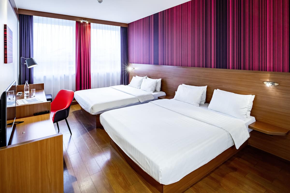 A hotel room with two beds, a desk, a chair, and a large window with curtains.