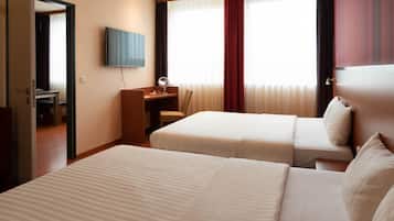 Una habitación de hotel con dos camas, un escritorio con una silla, un televisor y una ventana con cortinas.