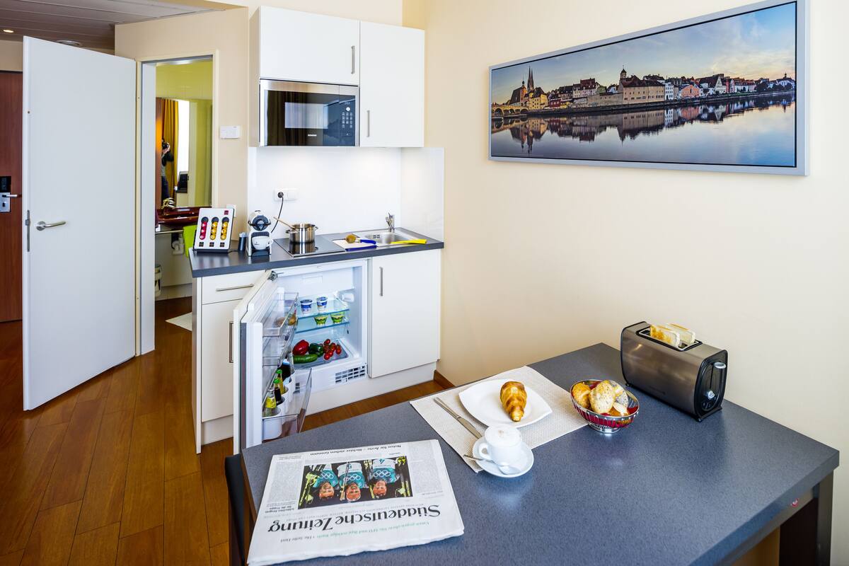 A compact kitchen with a microwave, refrigerator, and a small dining area with a toaster and croissant.