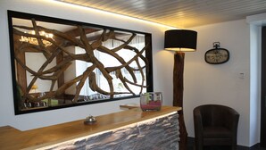 A reception area with a stone counter, a large mirror with a wooden frame, a lamp, a clock, and a chair. - Hotel de la Gare (Monthey)