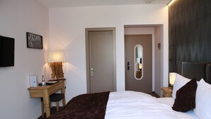 A hotel room with a bed, a desk, a chair, a lamp, a mirror, and a door. - Hotel de la Gare (Monthey)