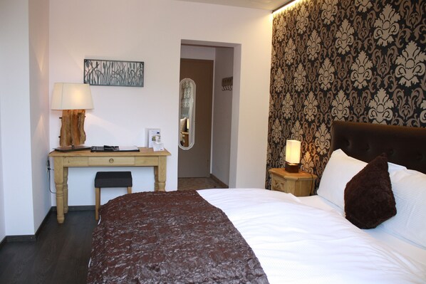 A hotel room with a bed, a desk, a chair, a lamp, a mirror, and a patterned wallpaper. - Hotel de la Gare (Monthey)