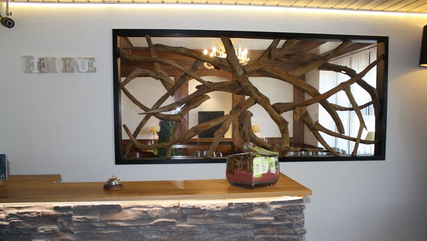 A reception desk with a stone base and a wooden top. Behind the desk, there is a wall-mounted mirror with a wooden frame. - Hotel de la Gare (Monthey)