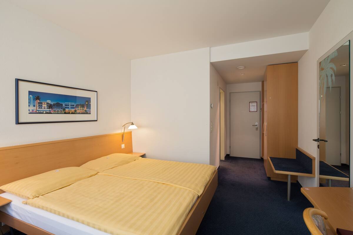 A hotel room with a bed, bedside table, lamp, and a framed picture on the wall.