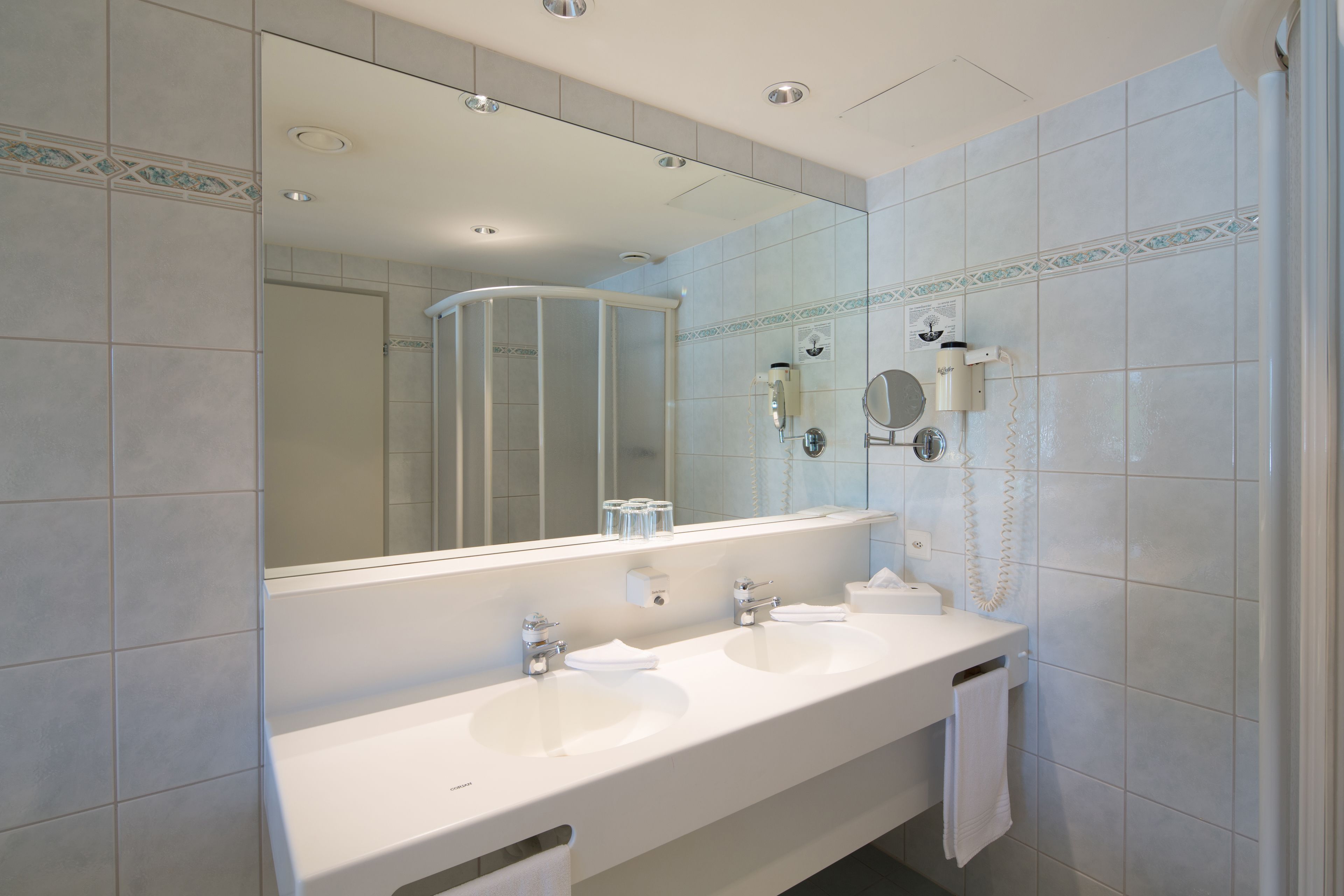 A bathroom with two sinks, a large mirror, and a shower enclosure.
